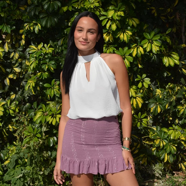 chica posando con una blusa cuello choker blanca sin mangas y falda de gomas corta rosa con hilo de lúrex plateado y volante en bajo