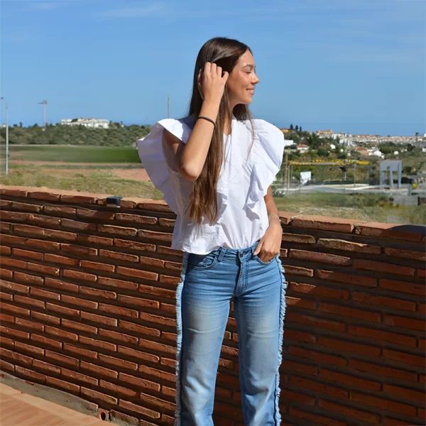 chica sonriendo con una Blusa blanca con volantes en manga corta y tejano azul con flecos en los laterales
