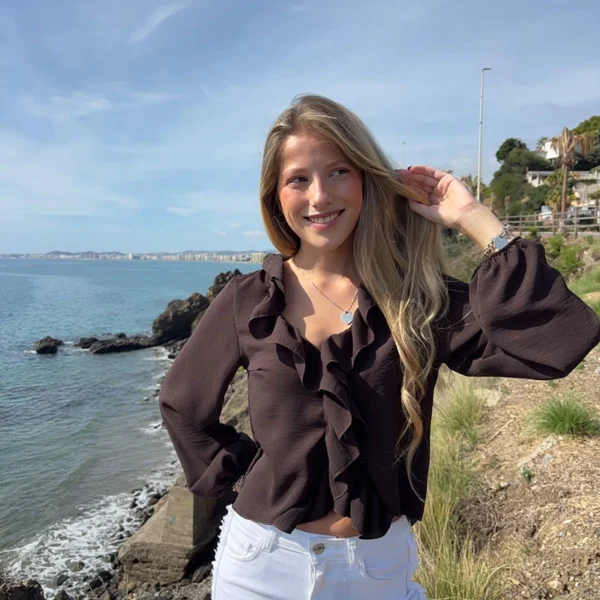 chica rubia posando en un acantilado con una blusa de color marrón chocolate con un volante alrededor del cuello y frontal