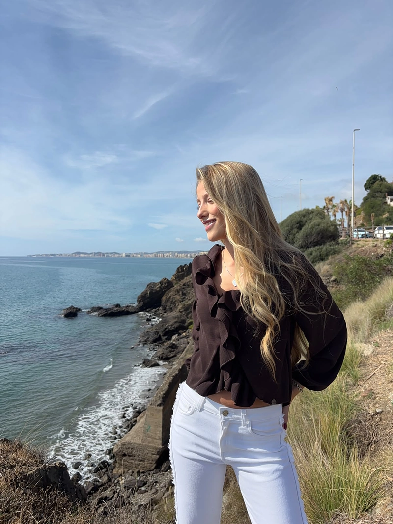 chica rubia posando en un acantilado con una blusa de color marrón chocolate con un volante alrededor del cuello y frontal