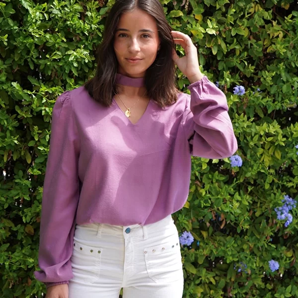 chica posando con una blusa rosa cuello pico y choker con un pantalón blanco