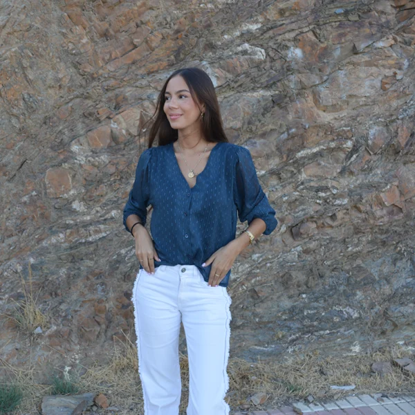 chica posando en el campo con un pantalón blanco con flecos laterales y una blusa azul mangas 3/4 con hilo de lúrex