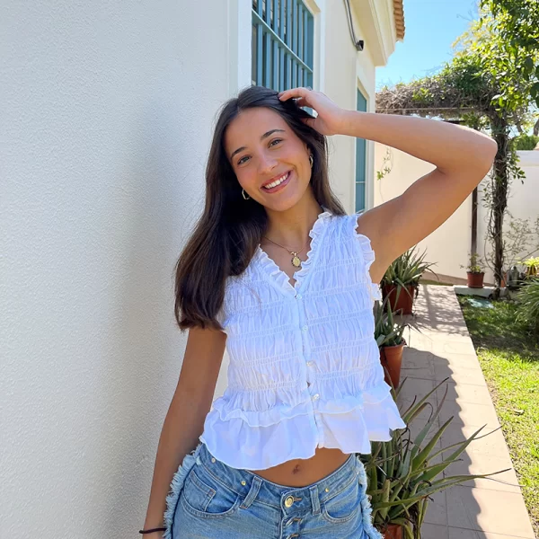 chica posando con una mano en el pelo vestida con una blusa sin mangas blanca fruncida y un short azul con flecos en los lados
