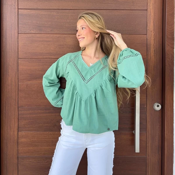 chica rubia posando delante de una puerta de madera con una blusa verde