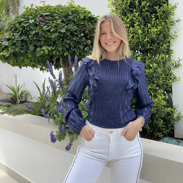 chica posando en jardín con una blusa azul marino con volantes y lineas de lurex dorado