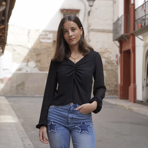 chica posando cvon una blusa negra de gasa con escote pico, manga larga, forro en frontal superior con un tejano azul con apliques de estrellas a sobre tono