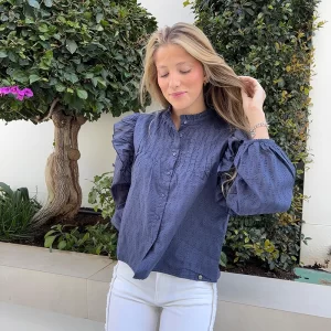 chica rubia posando con una blusa azul con volantes en los hombros