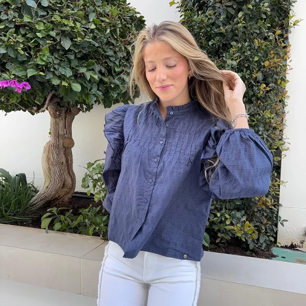 chica rubia posando con una blusa azul con volantes en los hombros