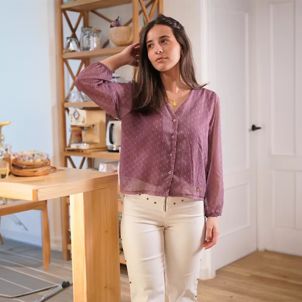 chica posando apoyada en un mueble de su salón con una blusa de gasa rosa con plumeti a tono y pantalón blanco con estrellas de tachuelas plateadas