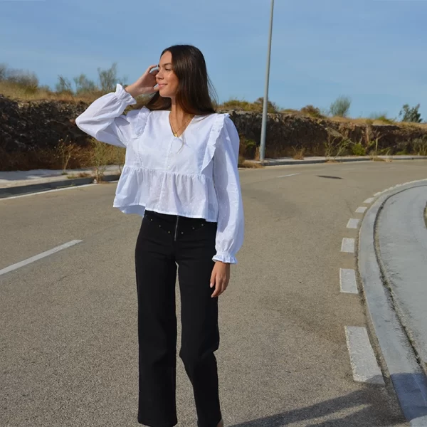 chica andando por la carretera con una blusa blanca de plumeti con volantes en sisas y pantalón negro con tachuelas de estrellas