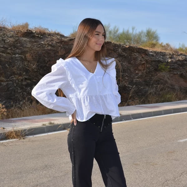 chica andando por la carretera con una blusa blanca de plumeti con volantes en sisas y pantalón negro con tachuelas de estrellas