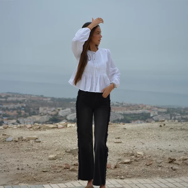 chica con una blusa blanca de manga larga cono tablas en el frontal y un pantalón negro con flecos en los lados