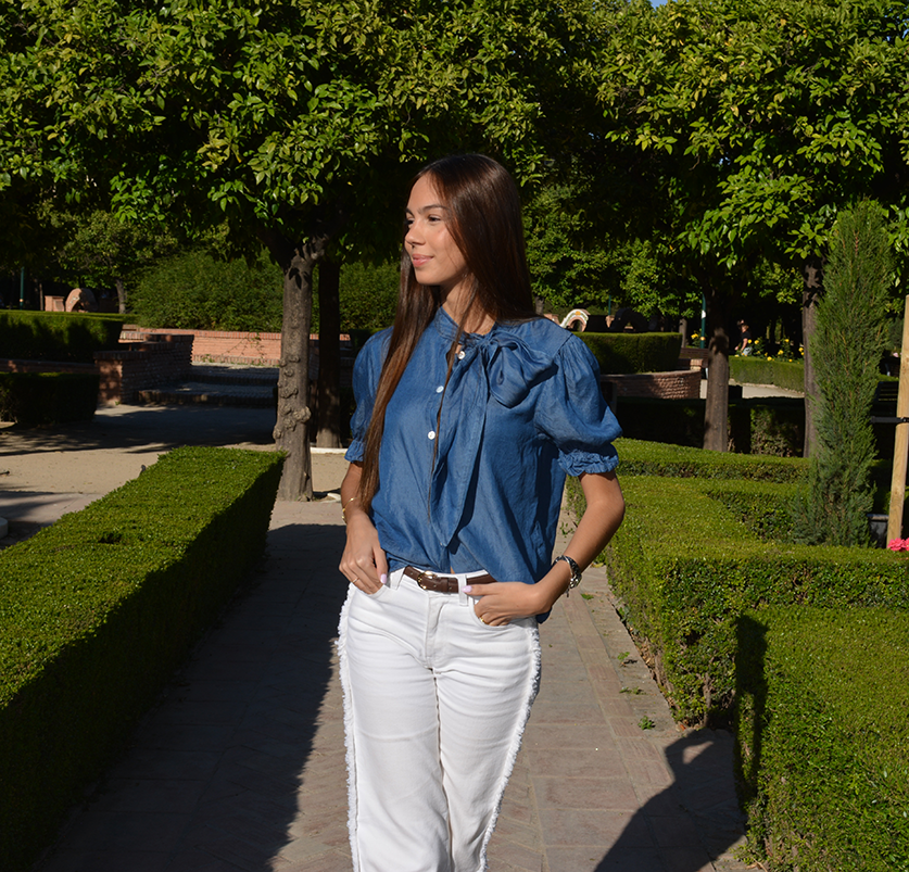 chica en un parque con un pantalón blanco con flecos en los laterales y blusa tejana manga corta con lazo en lateral del cuello