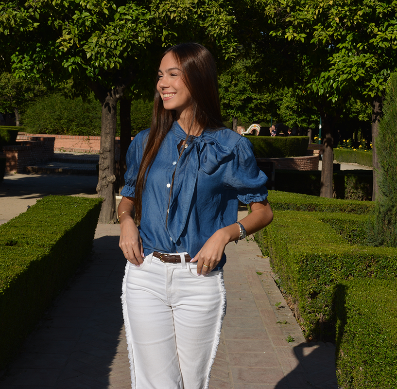 chica en un parque con un pantalón blanco con flecos en los laterales y blusa tejana manga corta con lazo en lateral del cuello