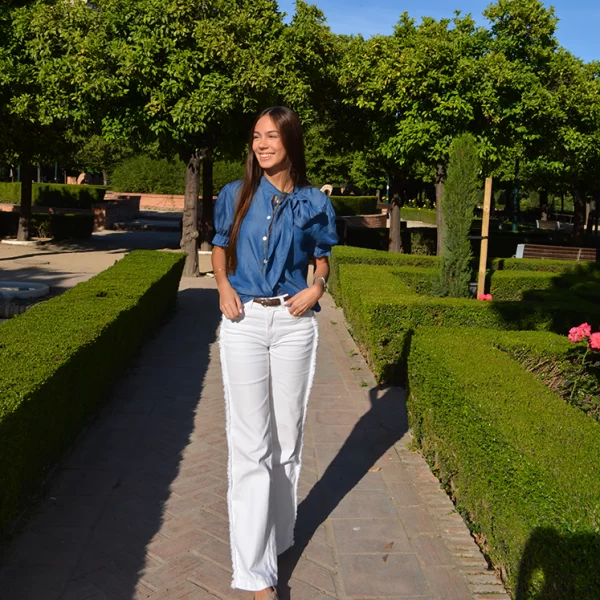 chica en un parque con un pantalón blanco con flecos en los laterales y blusa tejana manga corta con lazo en lateral del cuello
