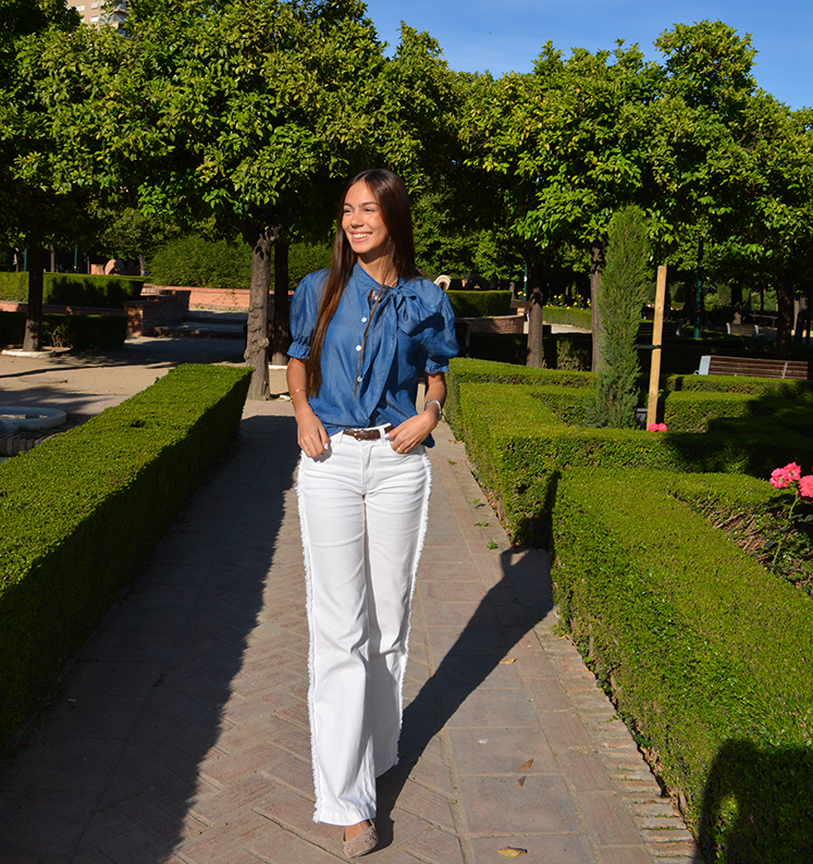 chica en un parque con un pantalón blanco con flecos en los laterales y blusa tejana manga corta con lazo en lateral del cuello