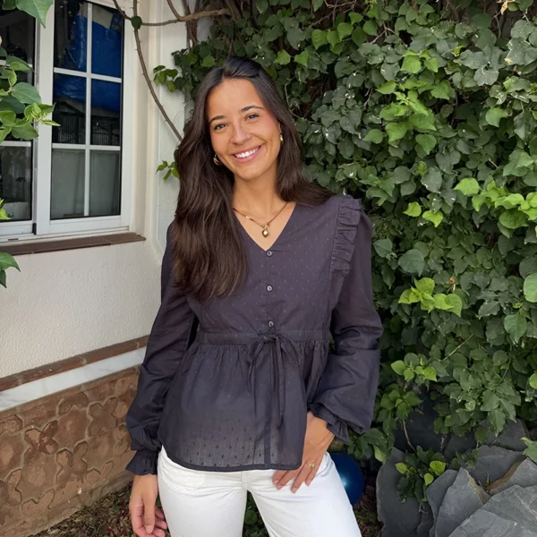 chica posando con una blusa antracita de plumetio con botonadura frontal y volantes en hombros. Cordón en cintura para ajustar