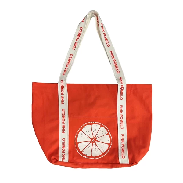 Bolso playero amplio, de tejido muy resistente, naranja con print blanco de texto Pink Pomelo en las asas y con rodaja de pomelo en bolsillo frontal. Cierre con clip. Bolsillo exterior en parte frontal.