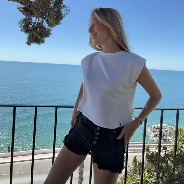 chica posando delante del mar con una camiseta blanca con un estampado de alas en color plateado en la espalda