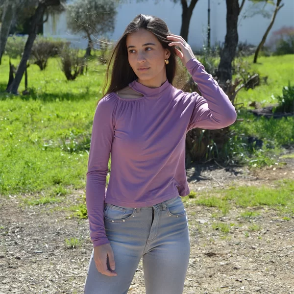 chica posando en un campo con una camiseta de manga larga rosa con cuello choker y hombro derecho descubierto y pantalón gris con tachuelas plateadas en bolsillos frontales
