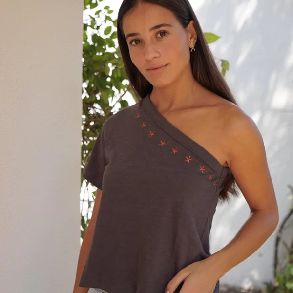 chica posando en un jardín con una camiseta asimétrica de color antracita con estrellas bordadas rojas