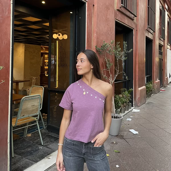 chica posando con camiseta asimetrica rosa con estrellas plateadas bordadas alrededor del cuello frontal