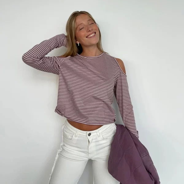 chica posando delante de una pared blanca con una camiseta manga larga con hombros descubiertos con rayas berenjena y blancas. 100% Algodón
