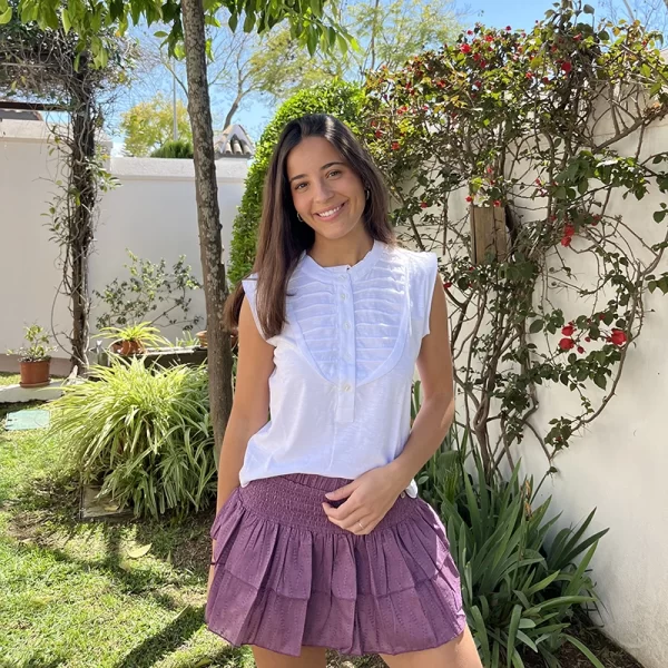 chica posando en jardin con una camiseta sin mangas blanca con pliegues y botones en el pecho