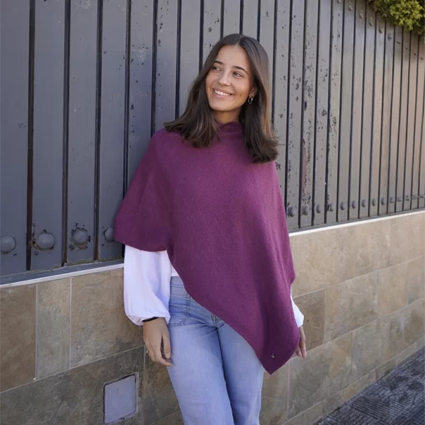 chica apoyada en un muro con vaya antracita con un pantalón tejano azul de pink pomelo y una capa berenjena