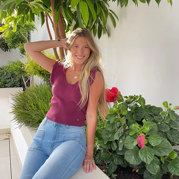chica sentada en una jardinera con un top berenjena de tricotosa con volantes en mangas y tejano celeste