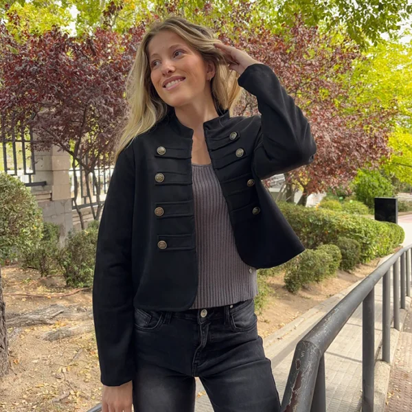 chica posando en un parque con una chaqueta negra de alamares con top gris y pantalón negro