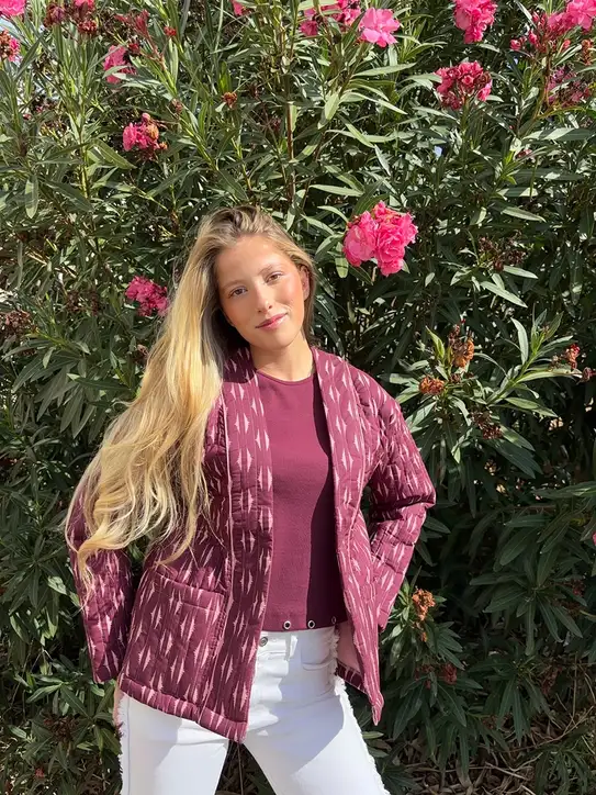 chica rubia posando delante de unas adelfas rosas con una chaqueta acolchada sin ciere en tonos berenjenas y rosas