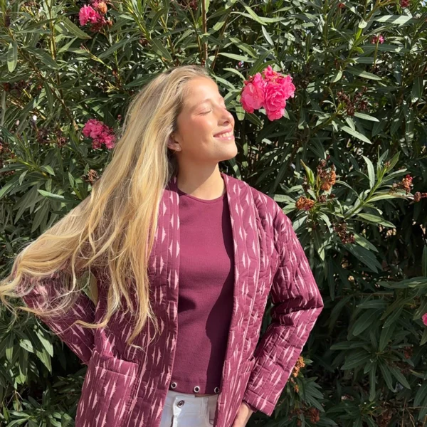 chica rubia posando delante de unas adelfas rosas con una chaqueta acolchada sin ciere en tonos berenjenas y rosas