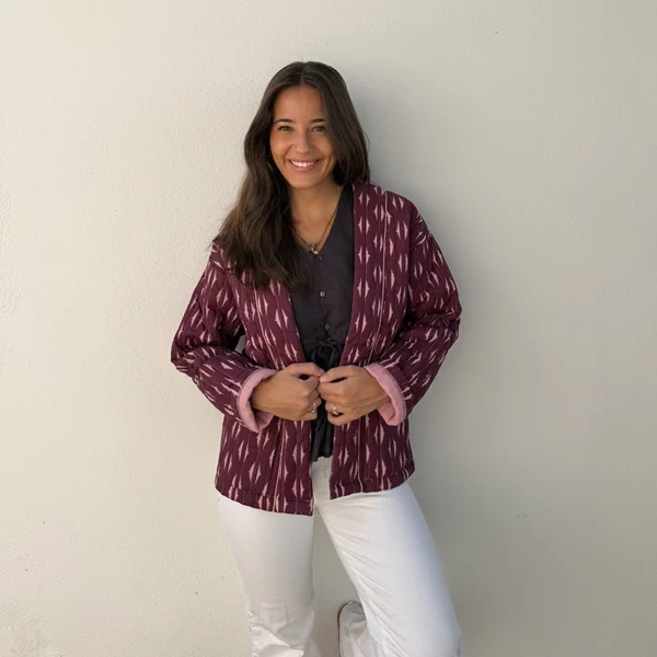 chica sonriendo con un pantalón blanco y chaqueta acolchada estampada en tonos burdeos