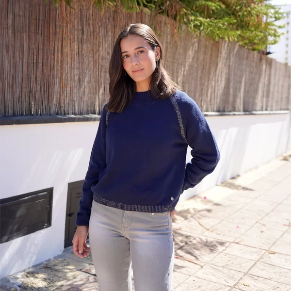 chica posando en la calle con un pantalón gris con tachuelas en los lados y un jersey azul marino con lurex dorado en hombros, bajo y puños