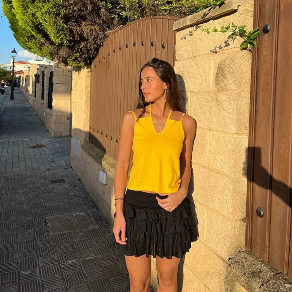 chica sonriendo con una camiseta de tirantes dobles en amarillo y una falda corta pantalón con 4 volantes en negra