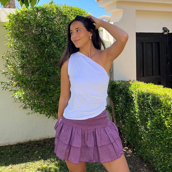 chica posando en un jardín con un top sin mangas asimétrico y falda pantalón corta rosa viejo con dos volantes
