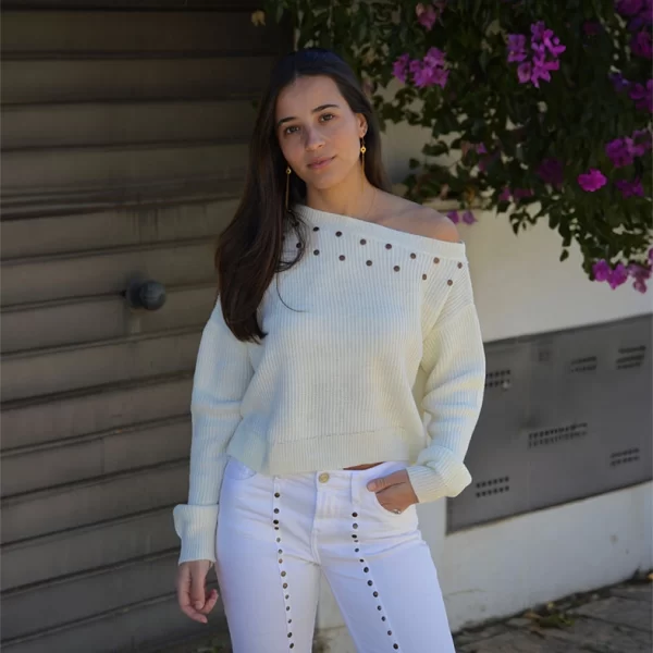chica con un jersey de pink pomelo crudo asimétrico descolgado en hombro izquierdo con tachuelas alrededor del escote frontal y pantalón blanco con tachuelas