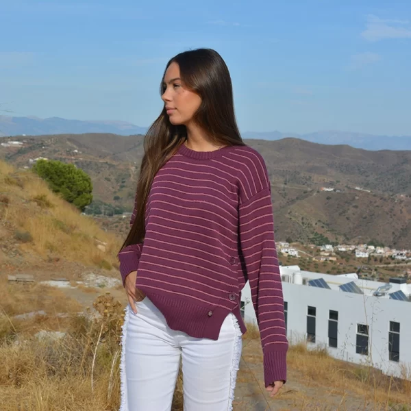chica mirando a un lado con un jersey de rayas en tonos burdeos y un pantalón blanco