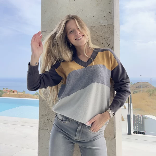 chica rubia posando al aire libre delante de una columna con un jersey cuello pico en tonos grises y mostaza