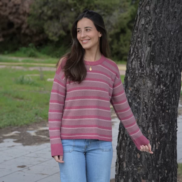 Chica posando en un parque delante de un árbol con jersey de rayas y hombros descubiertos en tonos rosas. Detalle de chapa metálica de Pink Pomelo en el bajo lateral izquierdo.