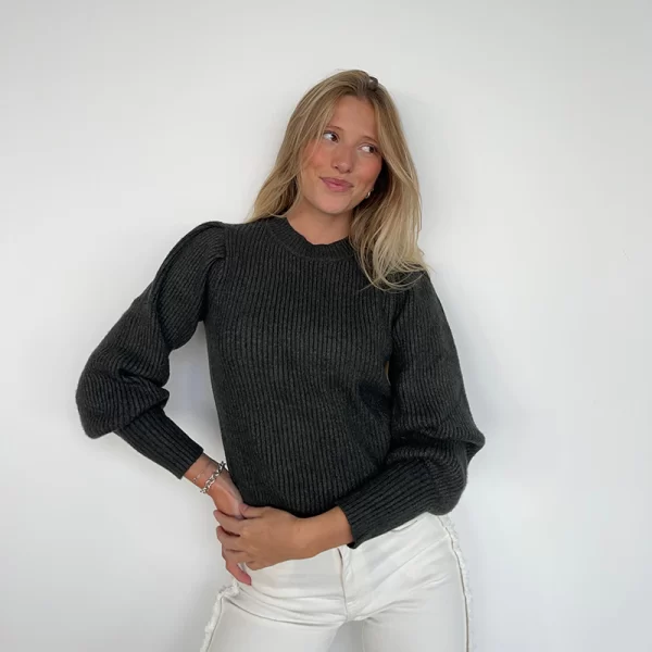 chica rubia posando delante de una pared blanca con un jersey cuello caja entallado y manga fruncida en el hombro