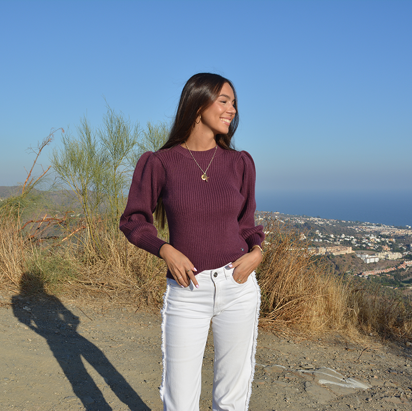 chica con un tejano blanco y un jersey berenjena de manga abullonado de tricotosa