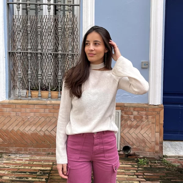 chica posando en la calle con un jersey blanco con hombro izquierdo descubierto y cuello choker. Los puños son ligeramente acampanados y lo lleva con un pantalón cargo rosa