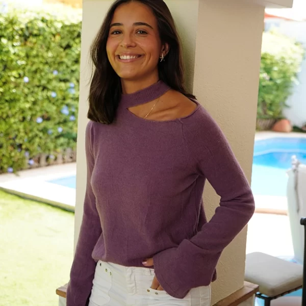 chica apoyada en una columna con un jersey rosa con cuello choker y hombro izquierdo descubierto