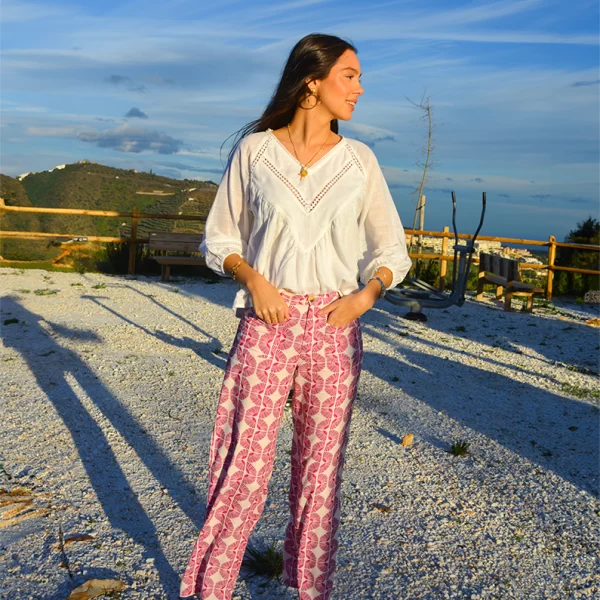 chica en un campo con las manos en los bolsillos delanteros de un pantalón largo fluido banco estampado en tonos frambuesas y blusa blanca