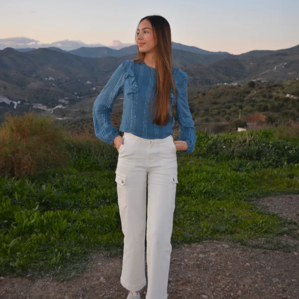 chica en el campo con un pantalón cargo blanco y una blusa azul con volantes en hombros
