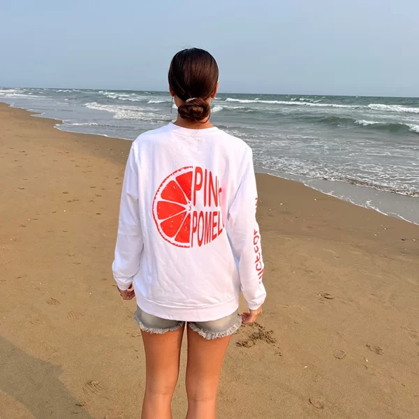 chica en la playa de espaldas con una sidadera blanca con print fluor