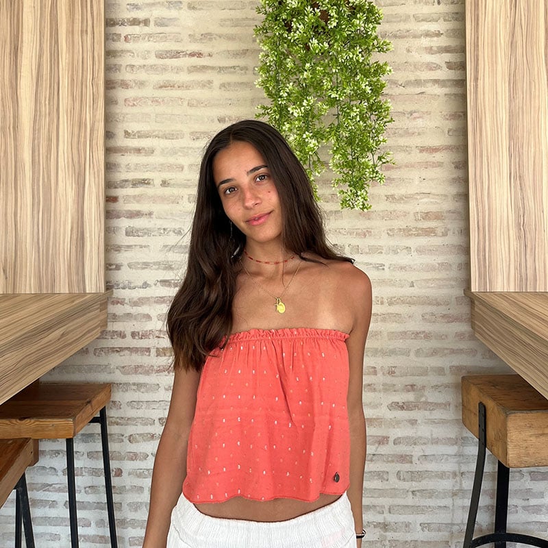 chica en un restaurante con un top palabra de honor naranja con goma elástica en interior de escote y círculos de hilos plateados y dorados