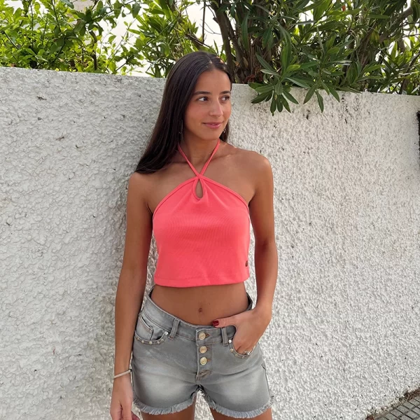 chica morena posando delante de un muro blanco con un top banda coral anaranjado atado al cuello y un short gris